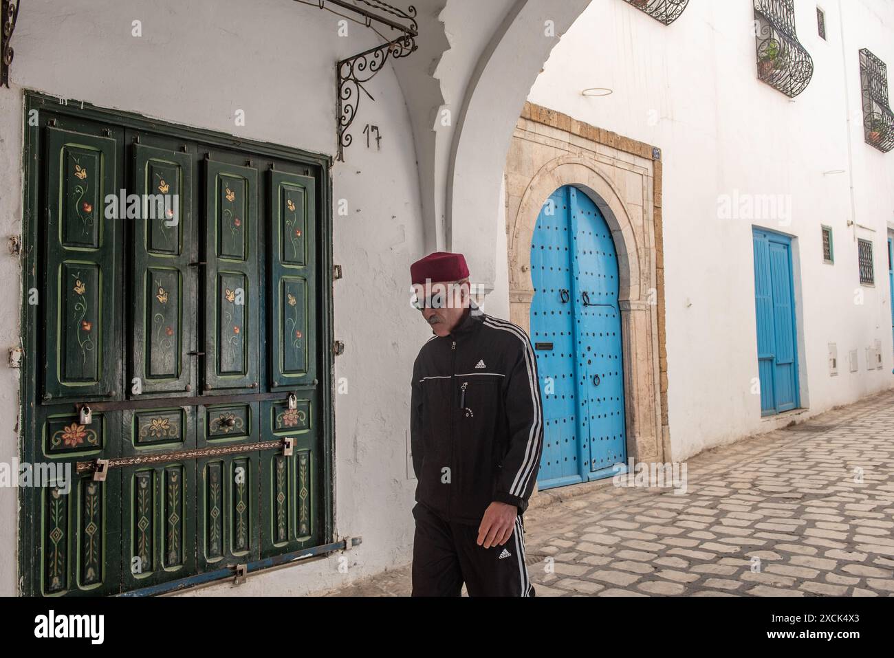 Tunisi, Tunisia 4 maggio 2024 Un tunisino che indossa un cappello rosso chechia nelle bellissime stradine di Tunisi Medina, un quar protetto dal Patrimonio Mondiale dell'Umanità Foto Stock