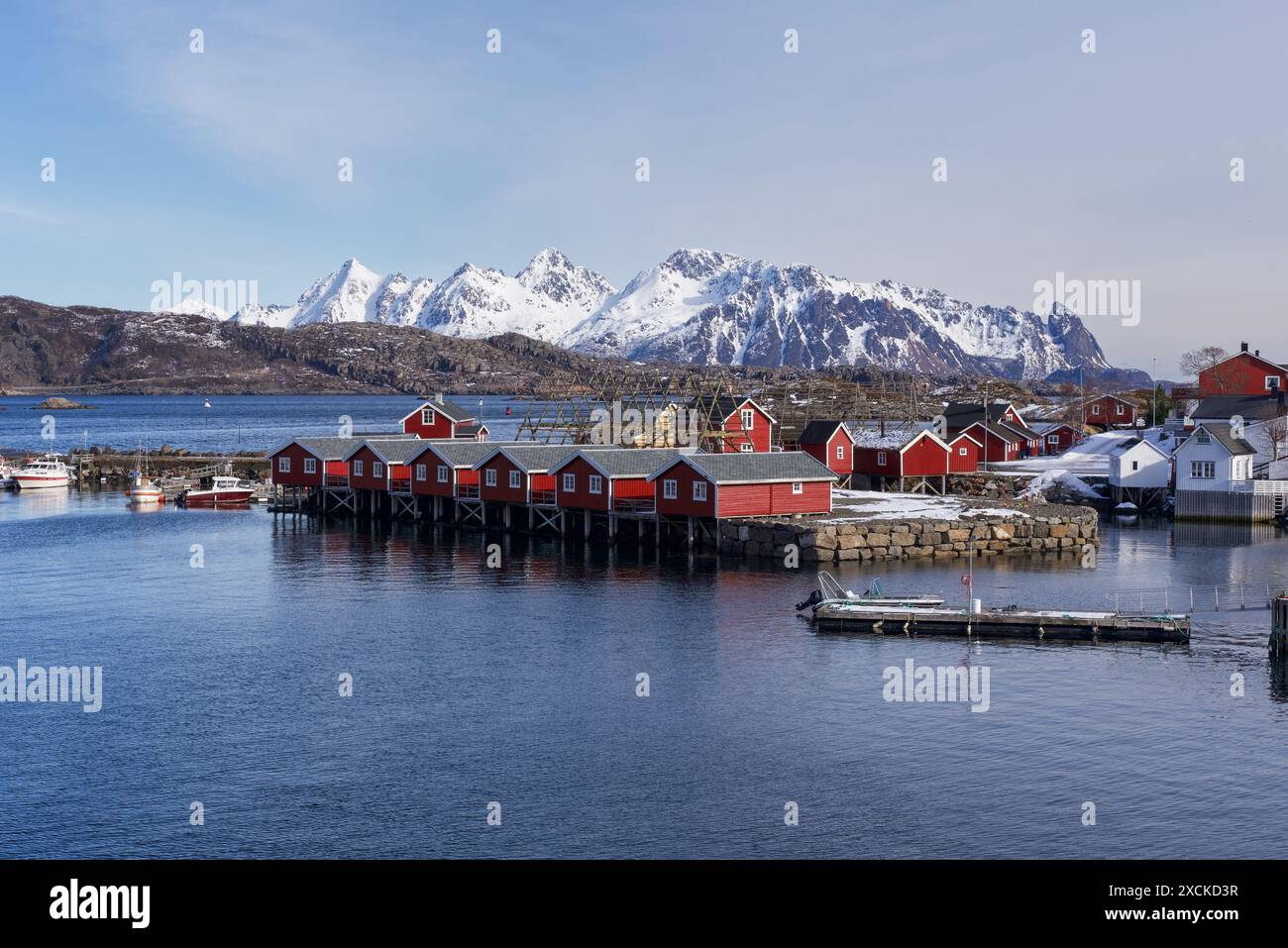 Svolvaer, isole Lofoten, Norvegia 03.28.2024 Vista sulle tradizionali cabine rosse dei pescatori rorbuer con montagne innevate sullo sfondo. Foto Stock