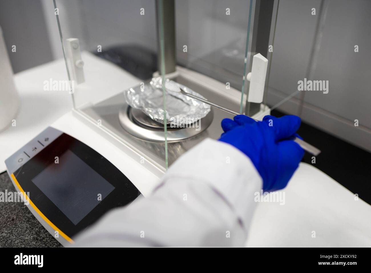 vista dettagliata della mano di uno scienziato che pesa un campione solido bianco su una scala Foto Stock