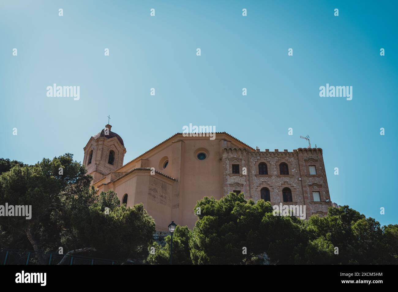 Un edificio storico con alberi in primo piano e un cielo azzurro. Castello di Cullera, Spagna Foto Stock