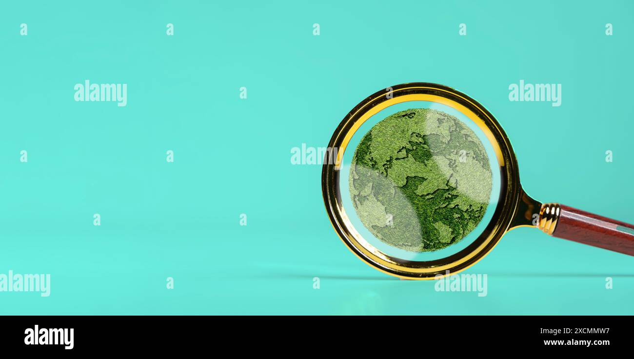 Lente di ingrandimento focalizzata sul globo digitale terrestre sull'erba su sfondo verde. Cooperazione commerciale per un ambiente sostenibile. Ambiente ESG S Foto Stock