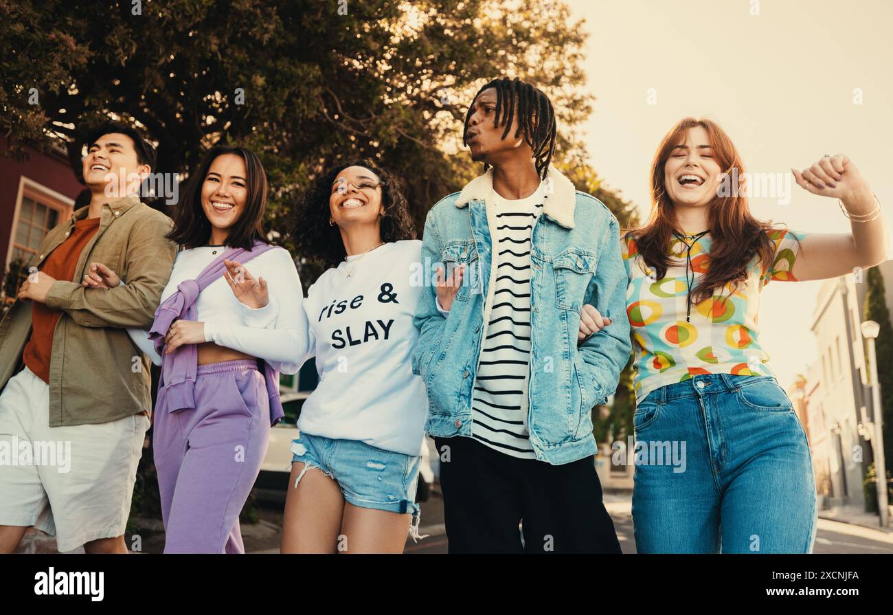 Un gruppo eterogeneo di amici che si diverte a passeggiare e ridere insieme in una giornata di sole, mostrando unità e felicità. Foto Stock