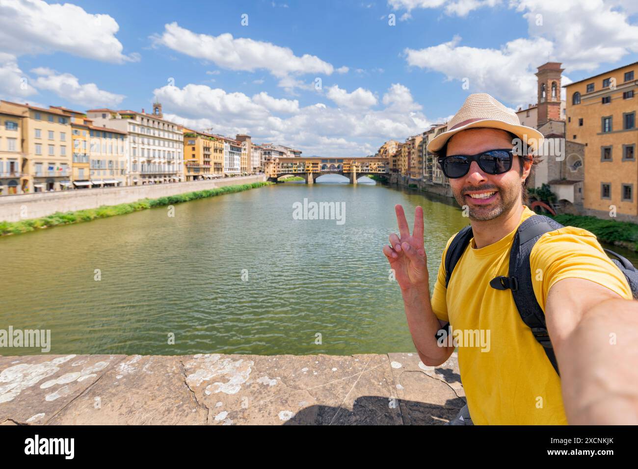 Il giovane gode di una splendida vista sul famoso Ponte Vecchio di Firenze, seduto sul lungofiume al tramonto. uomo viaggiatore in visita ai monumenti italiani. tr Foto Stock