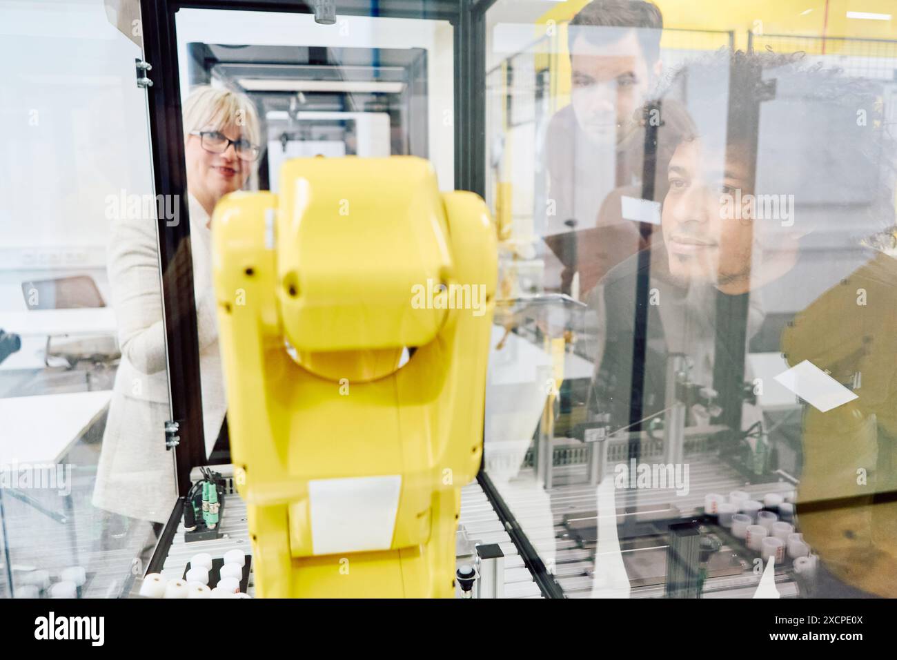 Gli ingegneri esaminano da vicino le funzionalità di un braccio robotico giallo durante una sessione di formazione pratica in un ambiente industriale. Foto Stock