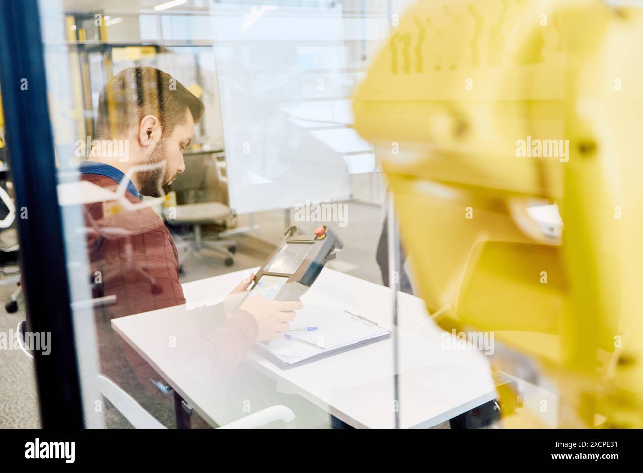 Un ingegnere lavora alla programmazione di un braccio robotico in un ambiente industriale, concentrandosi su automazione, produzione ed efficienza. Foto Stock