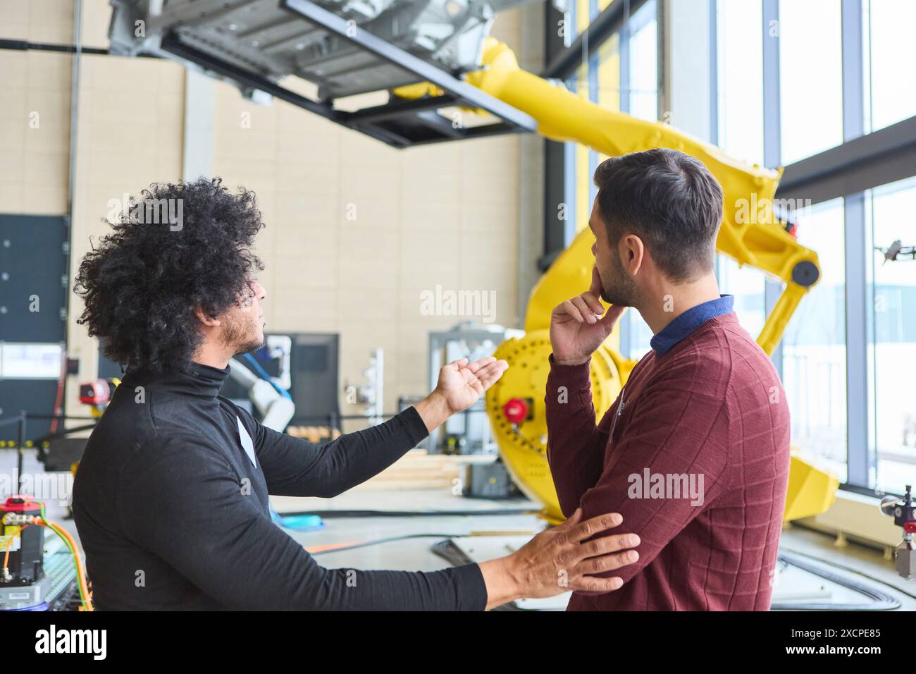 Due ingegneri sono impegnati in una discussione sui bracci robotici e sulle tecnologie di automazione all'interno di un ambiente industriale contemporaneo. Foto Stock