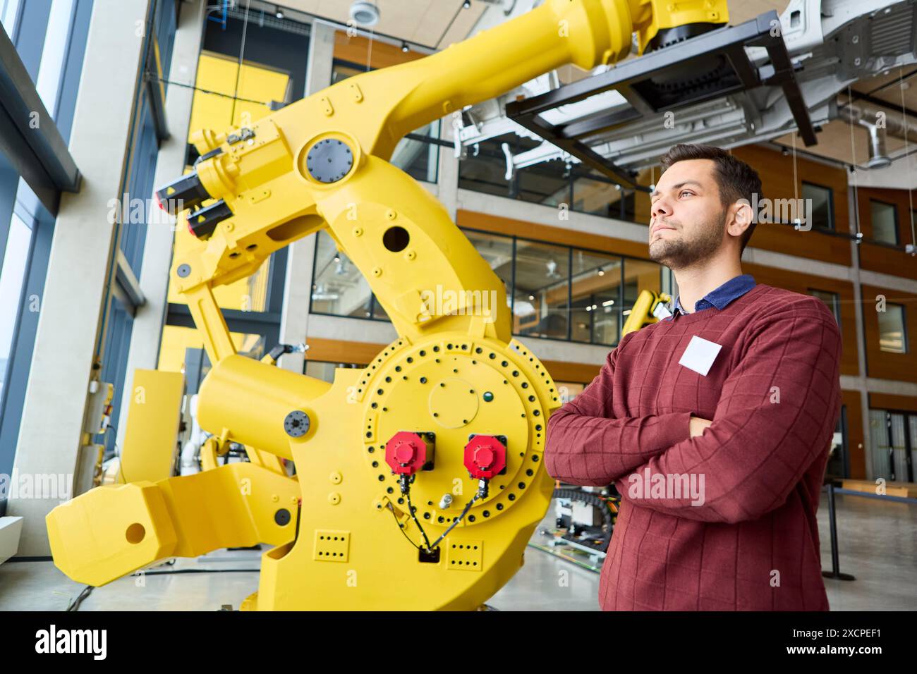 Ingegnere professionista che supervisiona un robot industriale avanzato con braccio di presa meccanico in un ambiente di produzione high-tech Foto Stock