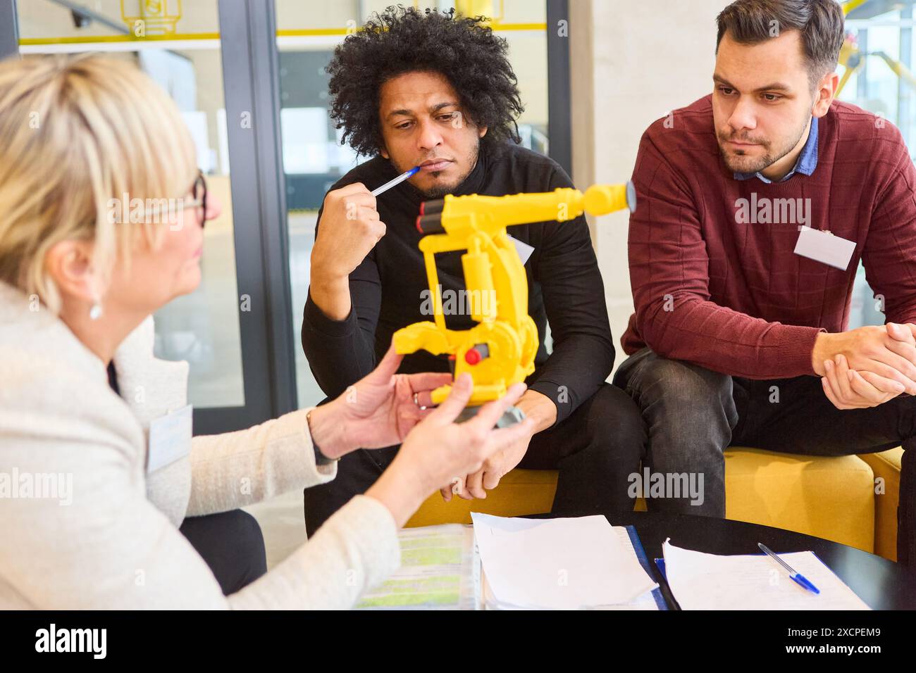 Un gruppo di ingegneri che discute dello sviluppo e della programmazione di un braccio di presa robotizzato, concentrandosi sull'automazione e sulle applicazioni industriali. Foto Stock