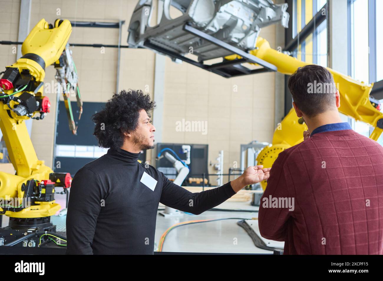 Gli ingegneri discutono della funzione e dell'applicazione di un robot industriale con braccio di presa, utilizzato per la produzione automobilistica in una moderna fabbrica Foto Stock