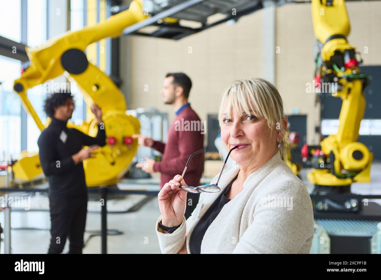 Ingegneri che discutono dello sviluppo e dell'automazione della robotica in un ambiente industriale moderno con bracci robotici e attrezzature avanzate. Foto Stock