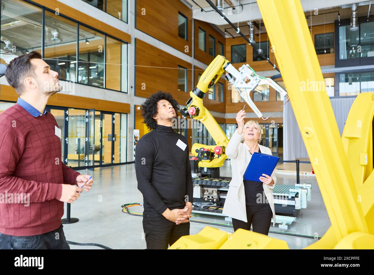 Team di ingegneri che collaborano e si addestrano alla programmazione di un braccio robotico per l'automazione in un moderno impianto industriale. Foto Stock