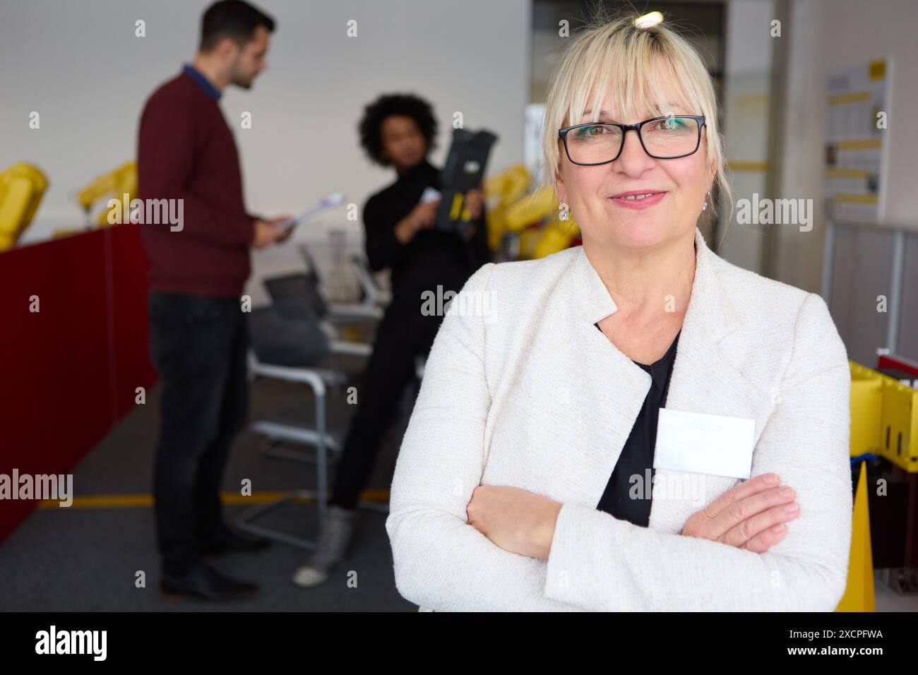 Donna d'affari sicura di sé in un ufficio moderno, concentrata sulla formazione in robotica, con colleghi che discutono in background. Rappresenta la leadership, Foto Stock