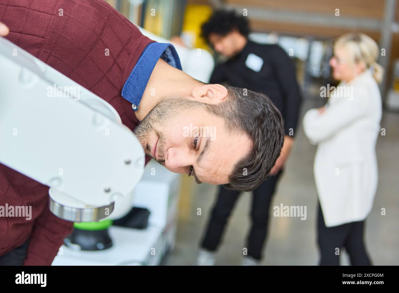 L'ingegnere esamina attentamente il braccio della pinza del robot durante una sessione di formazione pratica sulla robotica, con i colleghi in background, sottolineando l'auto del processo Foto Stock