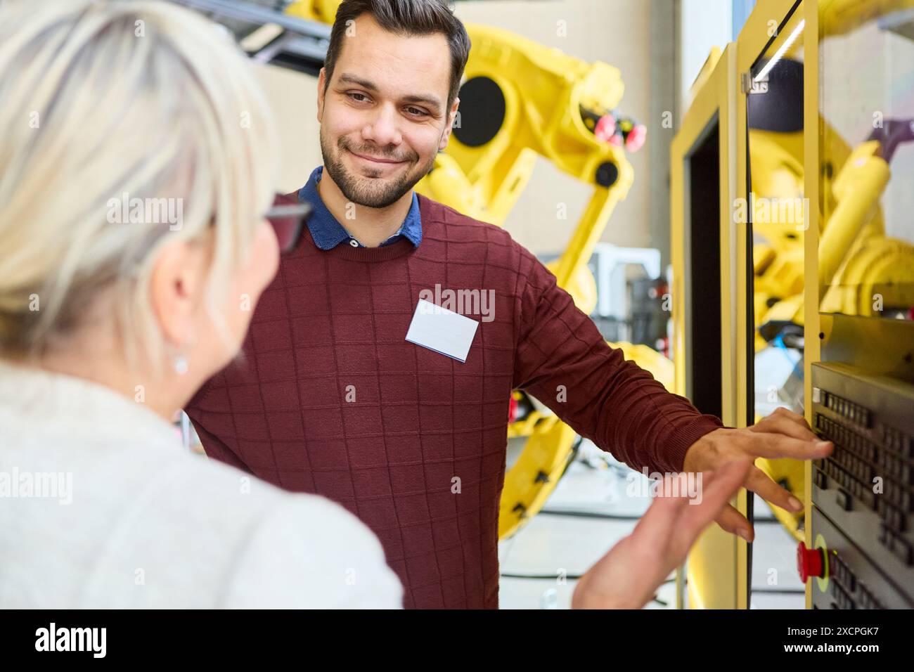 Ingegneri che hanno una conversazione durante la programmazione di un robot. L'immagine raffigura il lavoro di squadra e la tecnologia in un ambiente industriale. Foto Stock