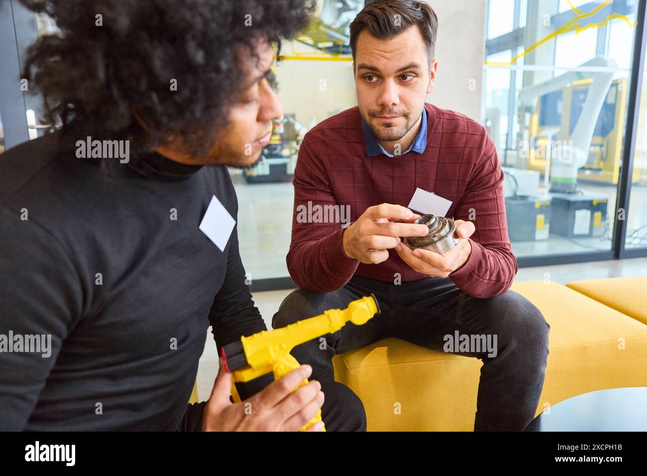 Due ingegneri esaminano e discutono parti di un braccio robotico in un ambiente industriale avanzato, concentrandosi sulla tecnologia e l'innovazione. Foto Stock