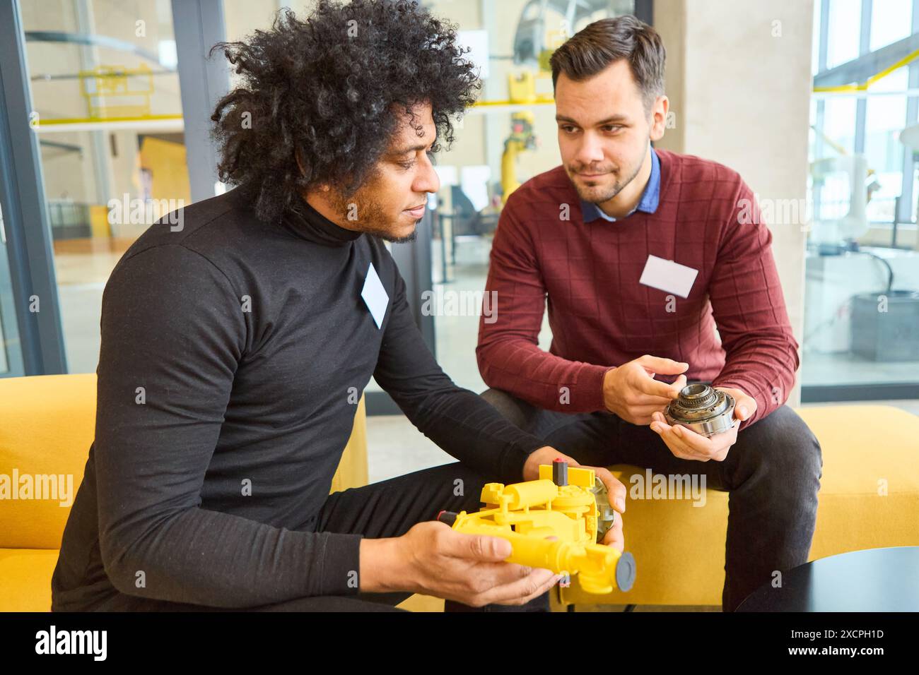 Due ingegneri si sono impegnati in una conversazione sulla robotica, tenendo in mano parti robotiche, evidenziando la formazione e la programmazione in un ambiente industriale. Foto Stock