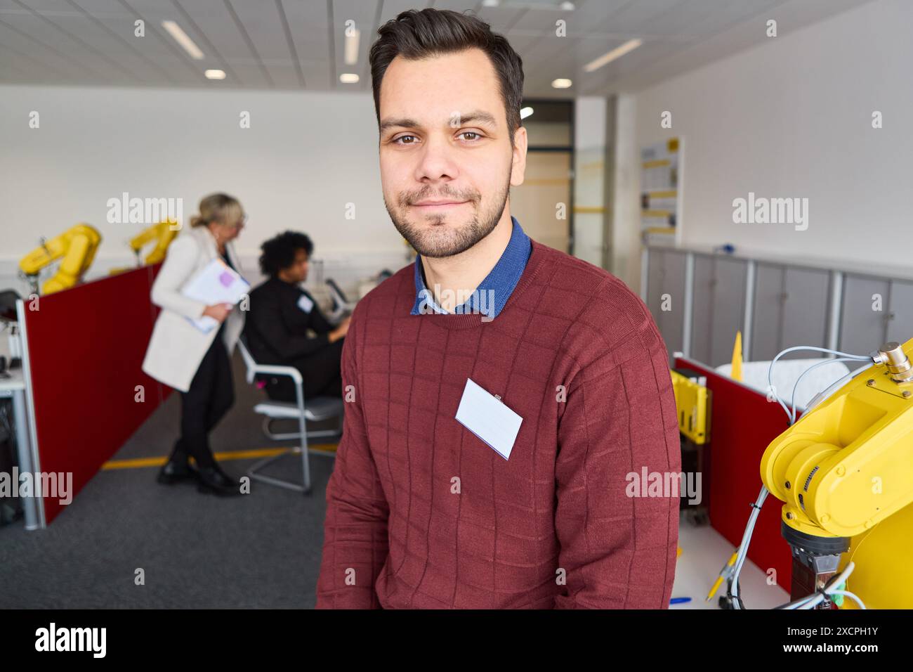 Giovane in un ambiente di formazione robotica con robot industriali sullo sfondo. Imparare a programmare e automatizzare i robot in un wor moderno Foto Stock