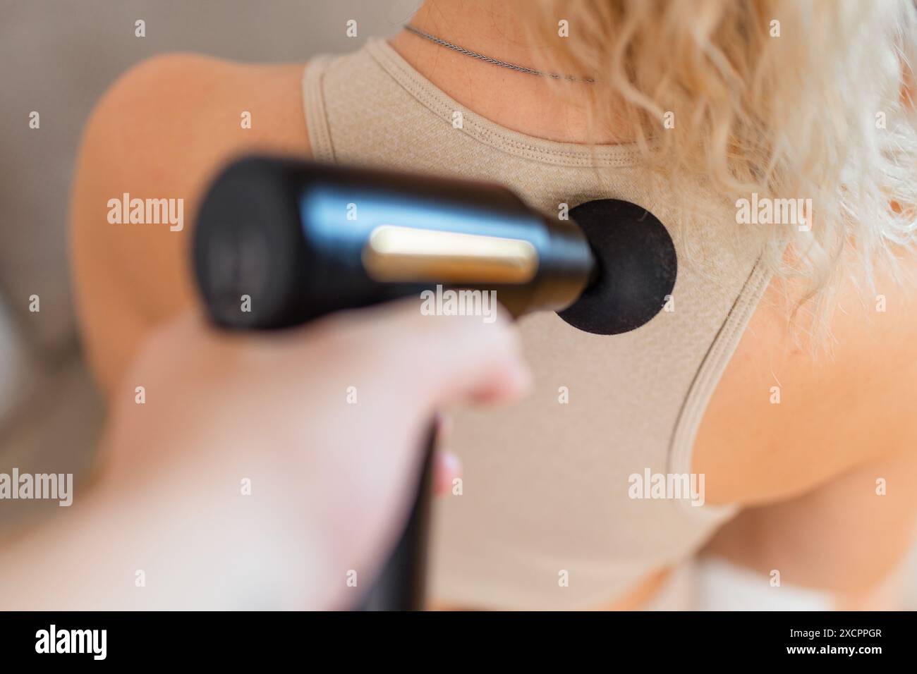 Ragazza a casa con una pistola massaggiante a percussione terapeutica in mano e massaggiando i muscoli della schiena concetto di recupero sportivo dopo un allenamento Foto Stock