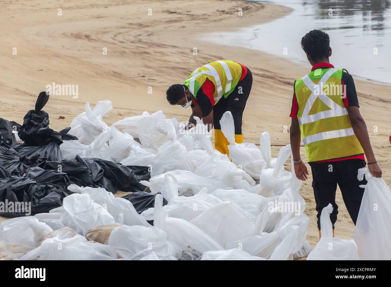 Due lavoratori legano la plastica dove fuoriesce petrolio contaminato lungo la costa di Palawan Beach, Sentosa. Singapore. Foto Stock