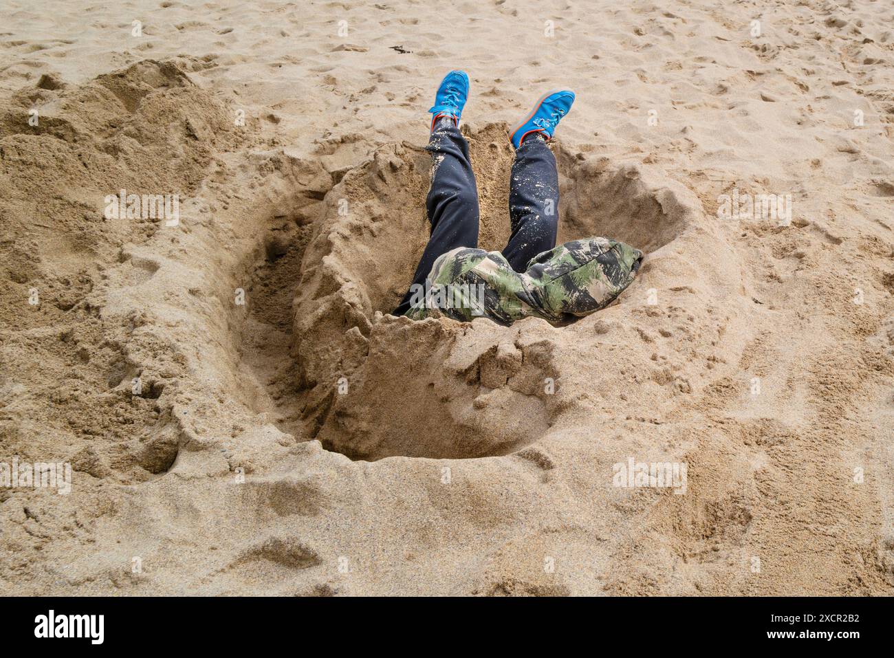Un giovane seduto e addormentato in un buco scavato nella sabbia su una spiaggia di Newquay, in Cornovaglia, nel Regno Unito. Foto Stock