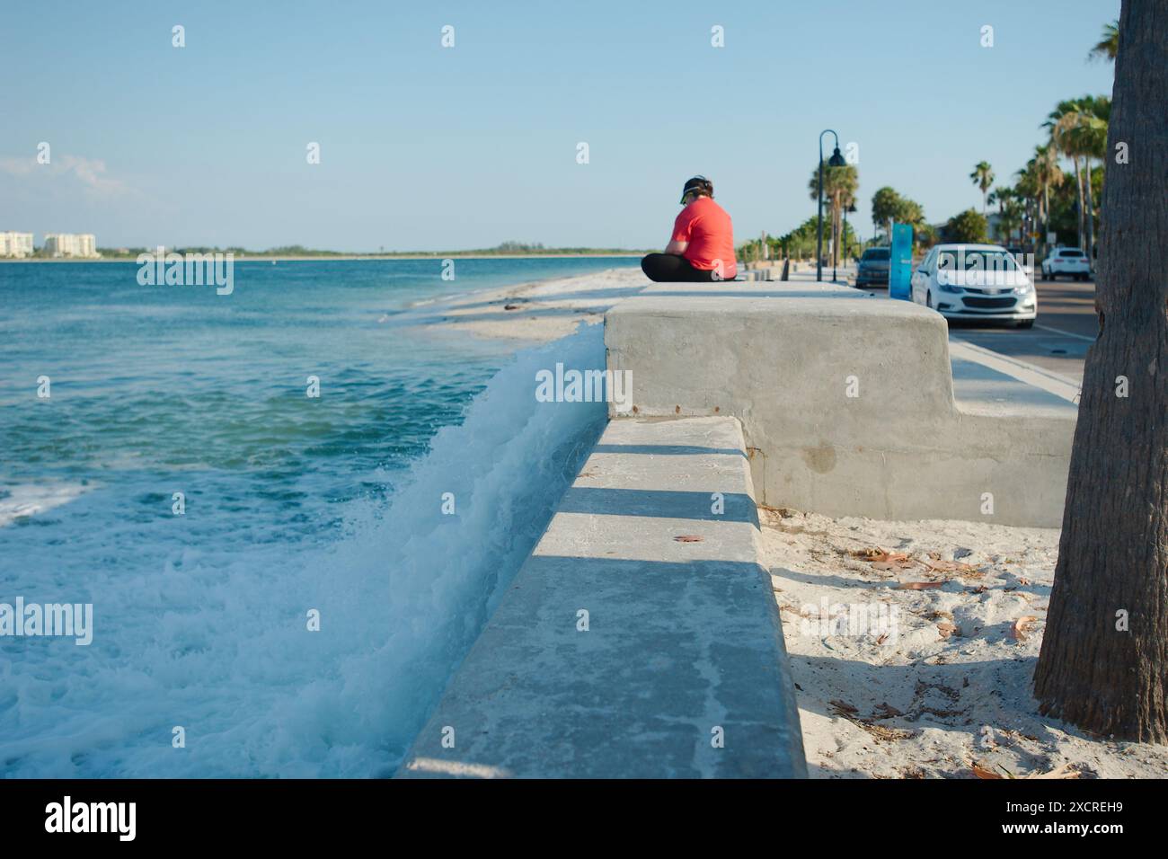 Vista media della stazione di sollevamento in calcestruzzo sulla destra con acqua che scorre velocemente. Donna seduta sulla camicia rossa destra. Quasi al tramonto con luce solare e ombra. Foto Stock