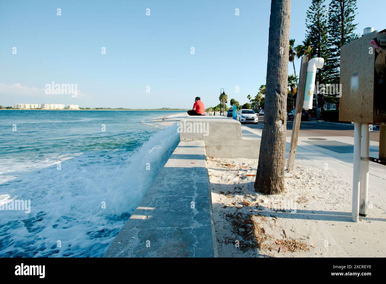 Ampia visuale della stazione di sollevamento in calcestruzzo a destra con acqua che fuoriesce velocemente. Donna seduta sulla camicia rossa destra. Quasi al tramonto con luce solare e ombra. Foto Stock