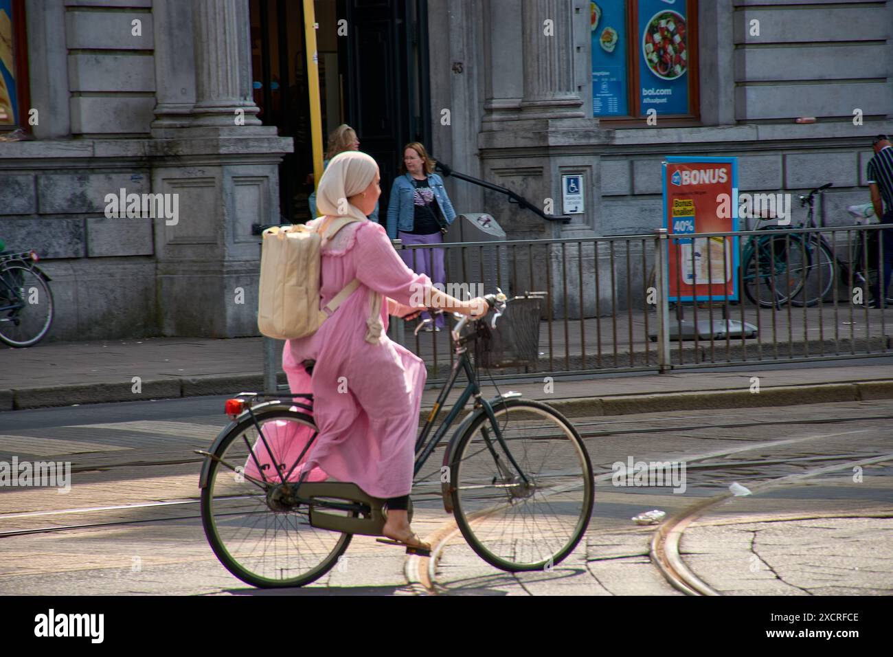 Anversa,Belgio;giugno,07,2024; donna musulmana in bicicletta vestita di rosa in tradizionale stile arabo con foulard Foto Stock