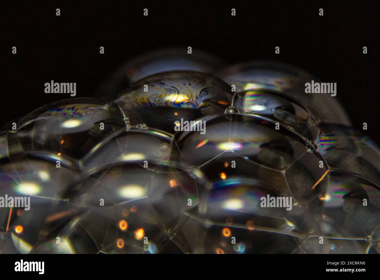 Macro astratta primo piano di bolle che soffiano più piccole bolle con sfondo nero e forme e riflessi colorati. Foto Stock