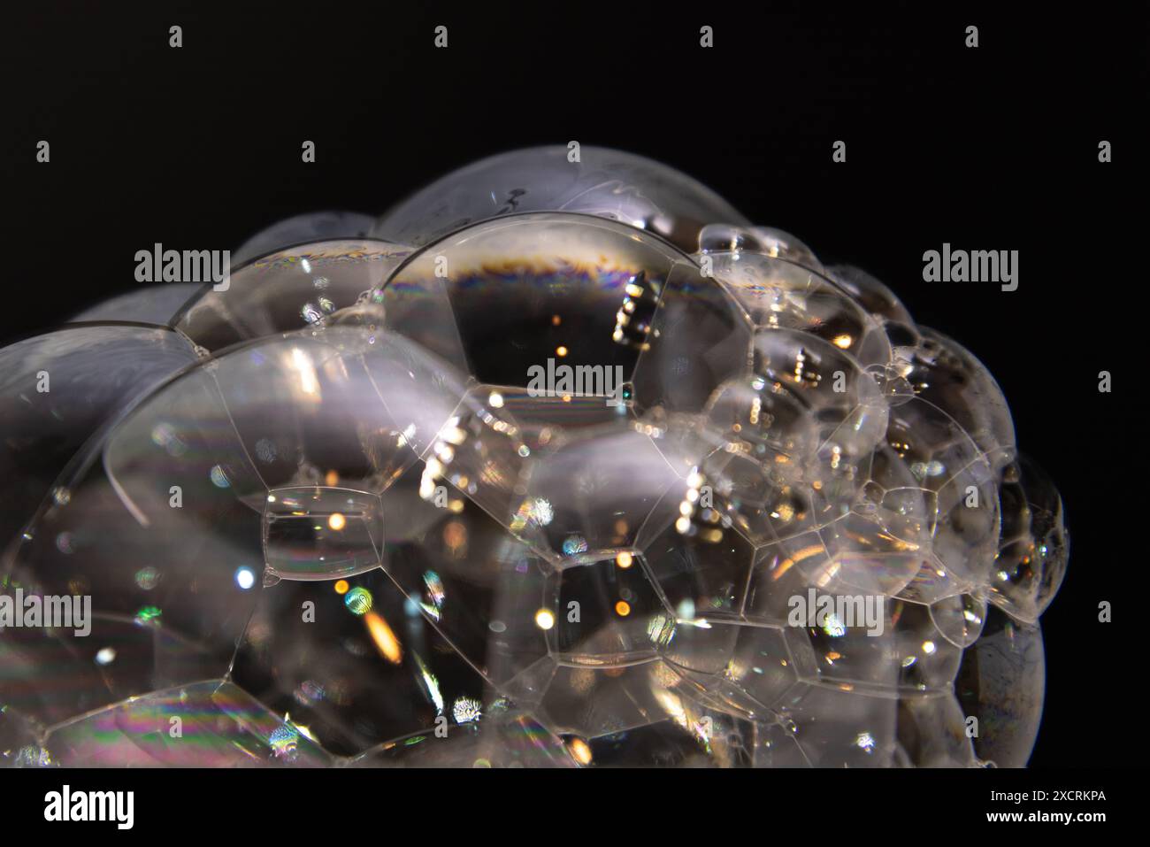 Macro astratta primo piano di bolle che soffiano più piccole bolle con sfondo nero e forme e riflessi colorati. Foto Stock