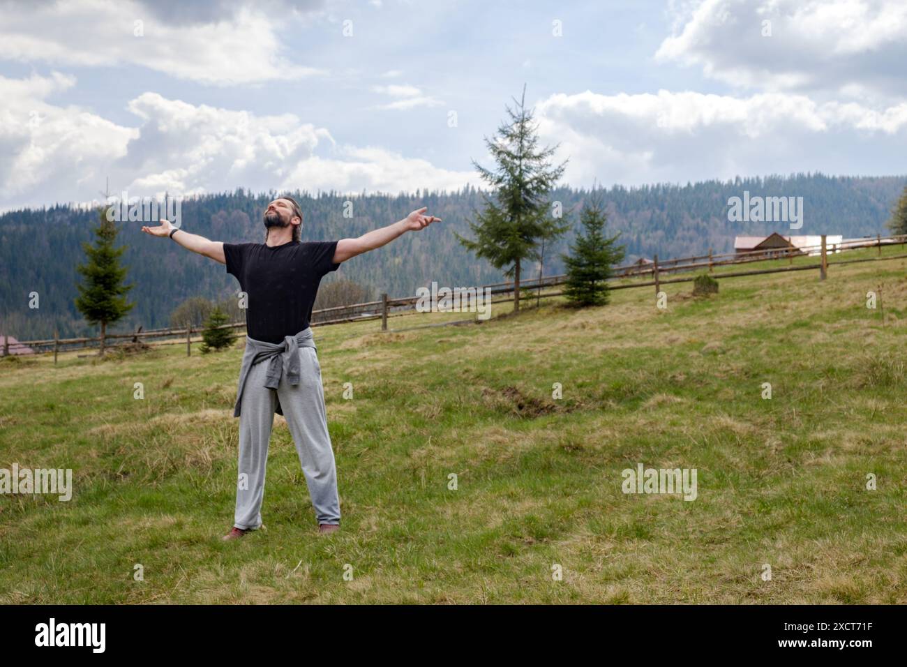 felice uomo caucasico in una radura sullo sfondo delle montagne. Ha sparso le braccia e chiuso gli occhi. concetto di unità con la natura e la mente h Foto Stock