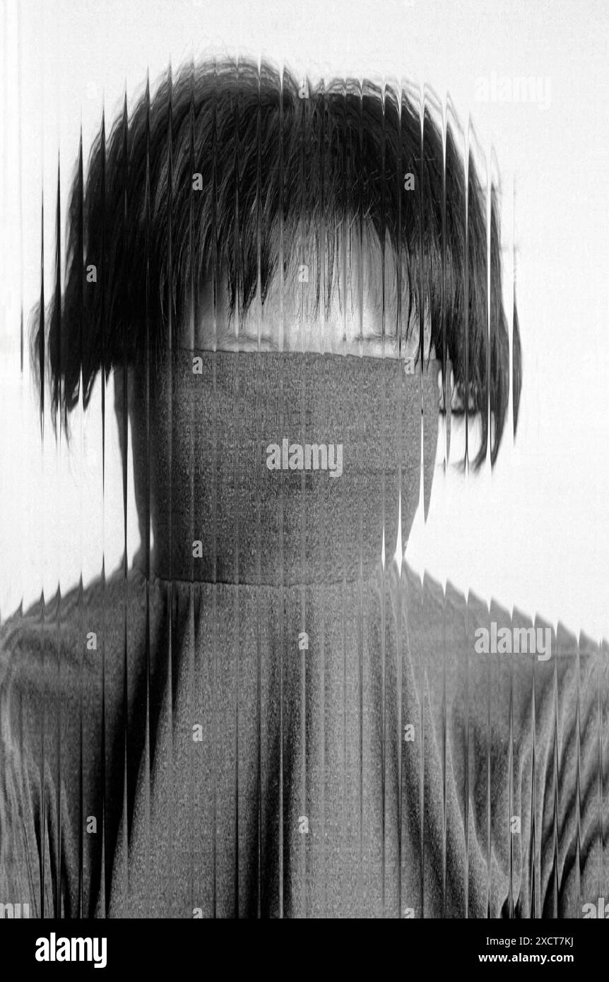 Un ritratto monocromatico di una timida donna asiatica dietro un fronte in vetro ondulato Foto Stock