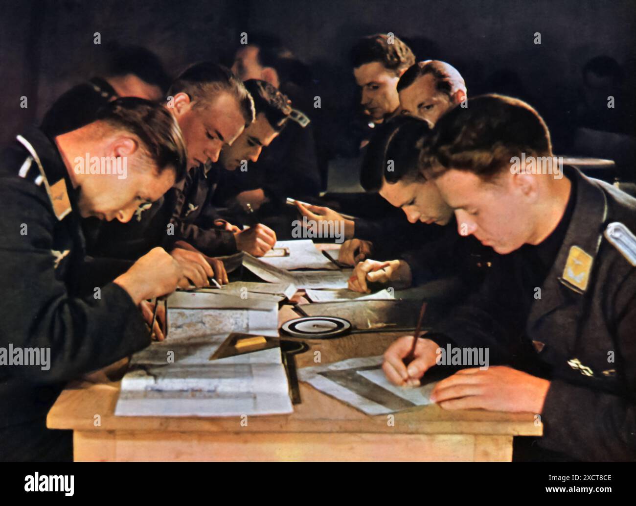 Una fotografia mostra i membri dell'Aeronautica militare tedesca, nota come Luftwaffe, che tracciano le loro rotte di volo utilizzando varie mappe e strumenti di navigazione, scattati durante la seconda guerra mondiale. Questi preparativi erano essenziali per garantire l'accuratezza e il successo delle loro missioni, che includevano ricognizione, bombardamenti e supporto aereo. Foto Stock