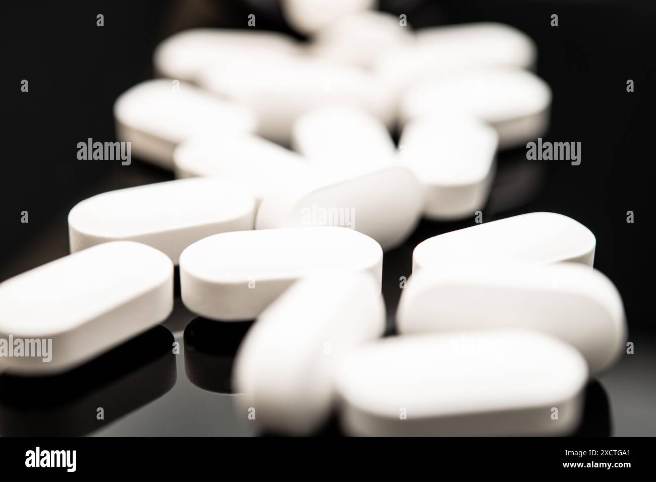 Uno scatto ravvicinato cattura numerose pillole ovali bianche sparse su uno sfondo scuro riflettente, evidenziando le preoccupazioni relative agli oppioidi come il fentanyl e. Foto Stock