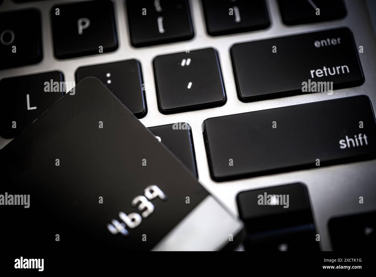 Un primo piano che cattura una carta di credito nera collocata su una tastiera portatile, che sottolinea le moderne tecnologie finanziarie e la sicurezza delle transazioni elettroniche, virus Foto Stock