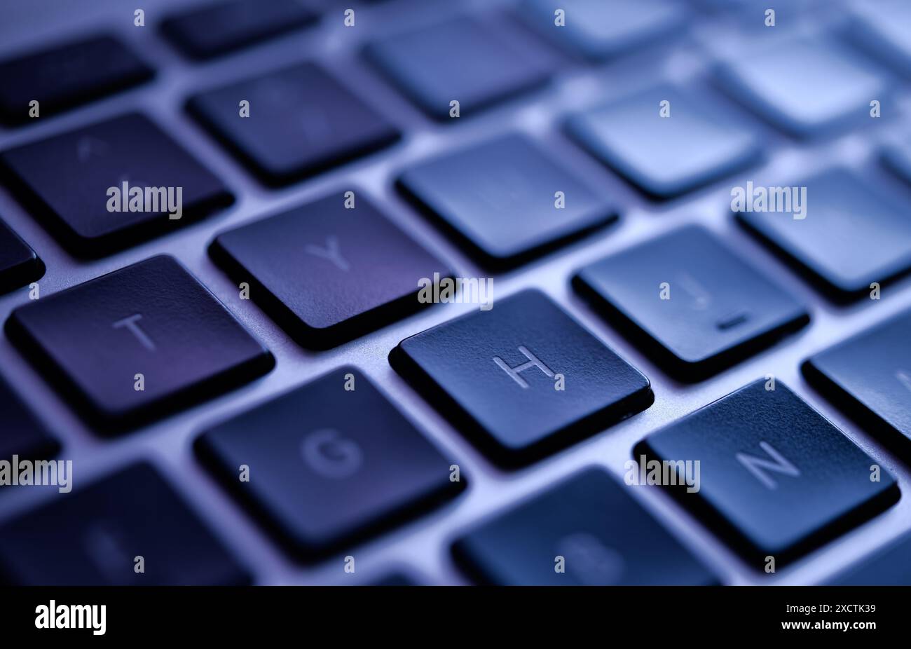 Primo piano di una moderna tastiera per notebook illuminata in blu, evidenziando potenziali violazioni di dati, minacce alla sicurezza informatica e vulnerabilità. Foto Stock