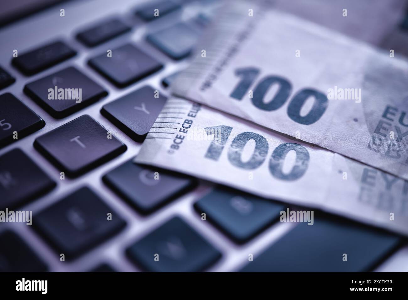 Una fotografia ravvicinata che cattura una banconota da 100 euro appoggiata su una tastiera di un computer portatile, sottolineando la finanza elettronica e le transazioni online, la criminalità informatica Foto Stock