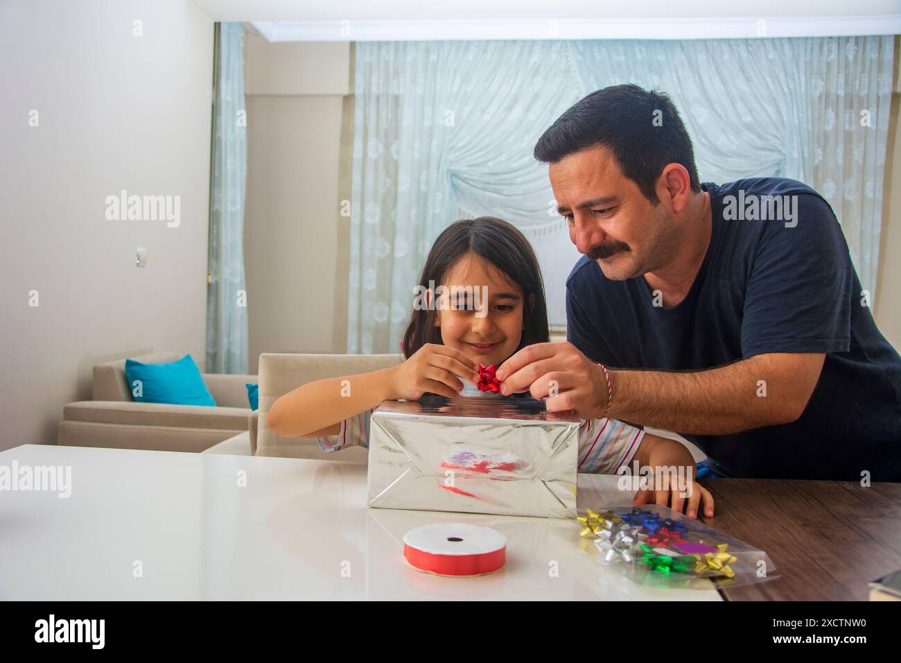 Il padre e la figlia che stanno aggiungendo decorazioni alla parte superiore della confezione regalo dopo aver preparato la confezione regalo Foto Stock