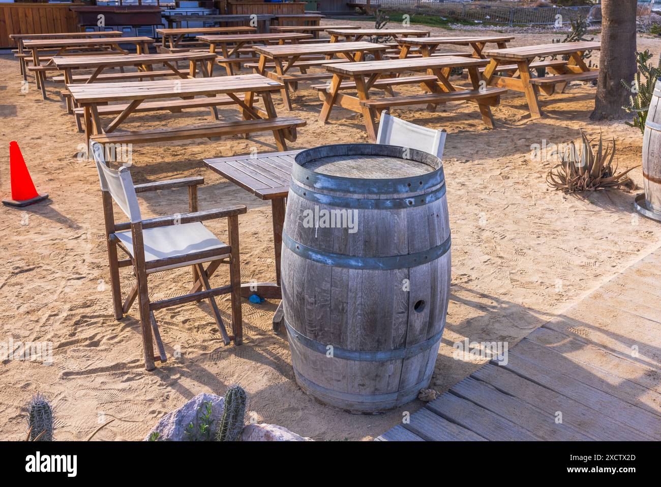 Splendida vista su un ristorante esterno vuoto con tavoli in legno, sedie e un tavolo a botte su una superficie sabbiosa. Curacao. Foto Stock