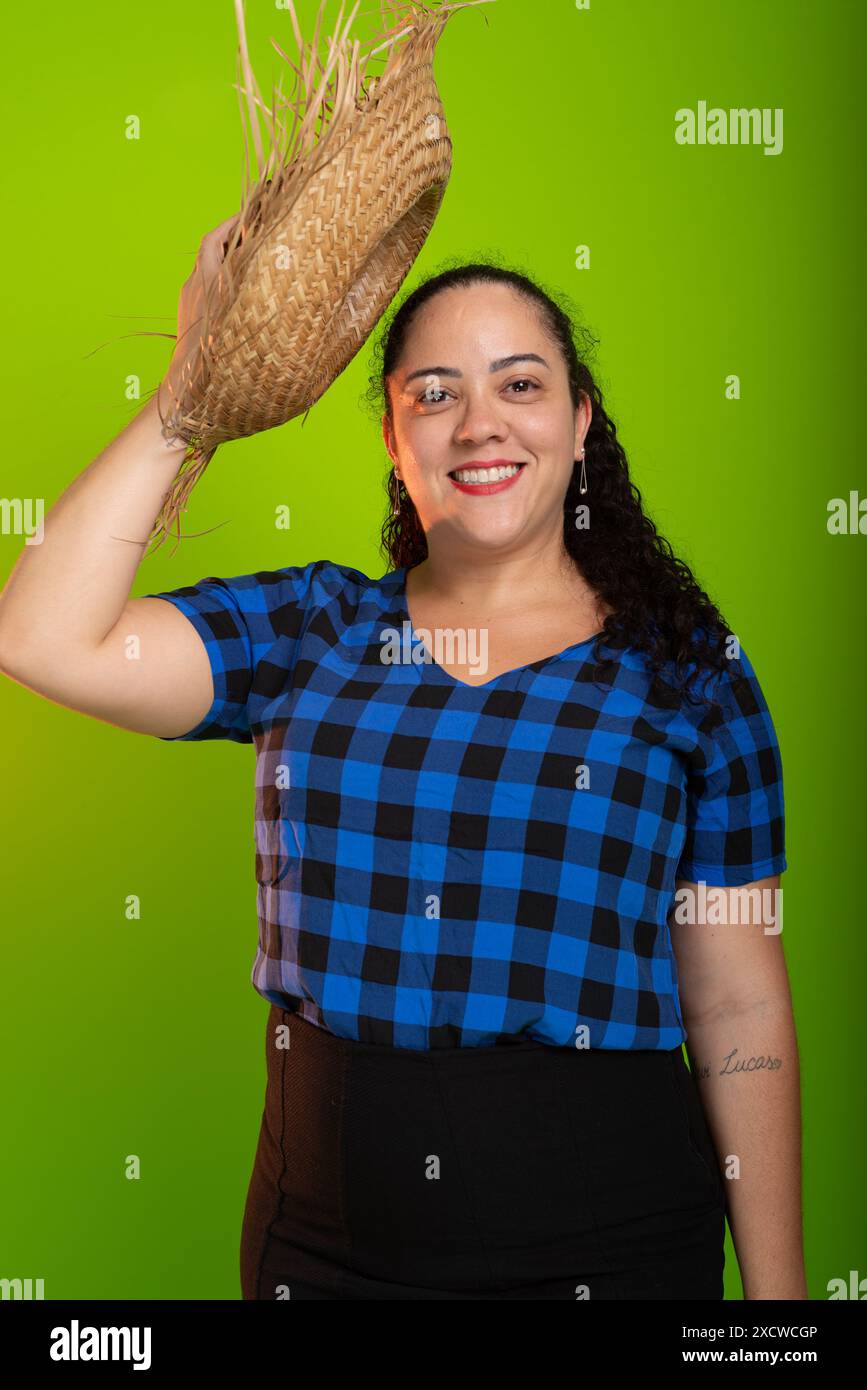 Giovane donna vestita di carattere per il festival di Sao Joao, che le mette un cappello di paglia sulla testa. Isolato su sfondo verde. Foto Stock