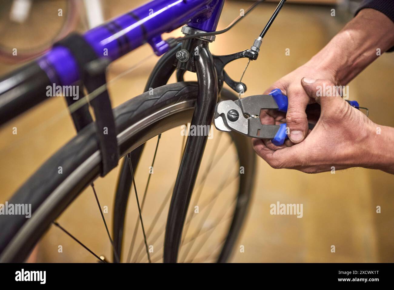 Il riparatore stringe il tappo sull'estremità di un cavo per bicicletta con un attrezzo crimpatore nella sua officina di riparazione. Composizione in primo piano con messa a fuoco selettiva e copia Foto Stock