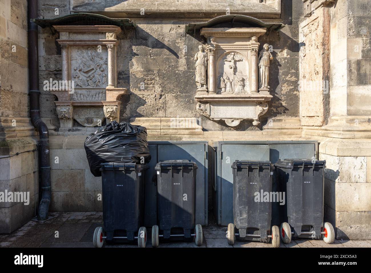 Vienna, Austria - 12 maggio 2024: Contenitori di rifiuti impilati contro le mura medievali della chiesa. Nessuna persona visibile Foto Stock