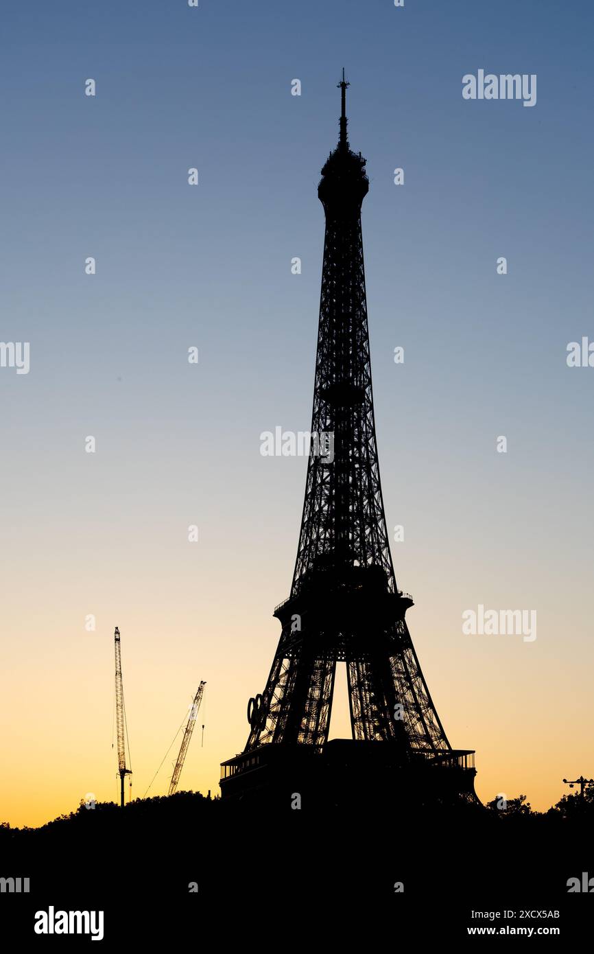 Parigi, Francia - 07 giugno 2024: Sagoma della Torre Eiffel alla luce del mattino presto. Logo dei giochi olimpici montato sulla torre e gru da costruzione a terra. Foto Stock