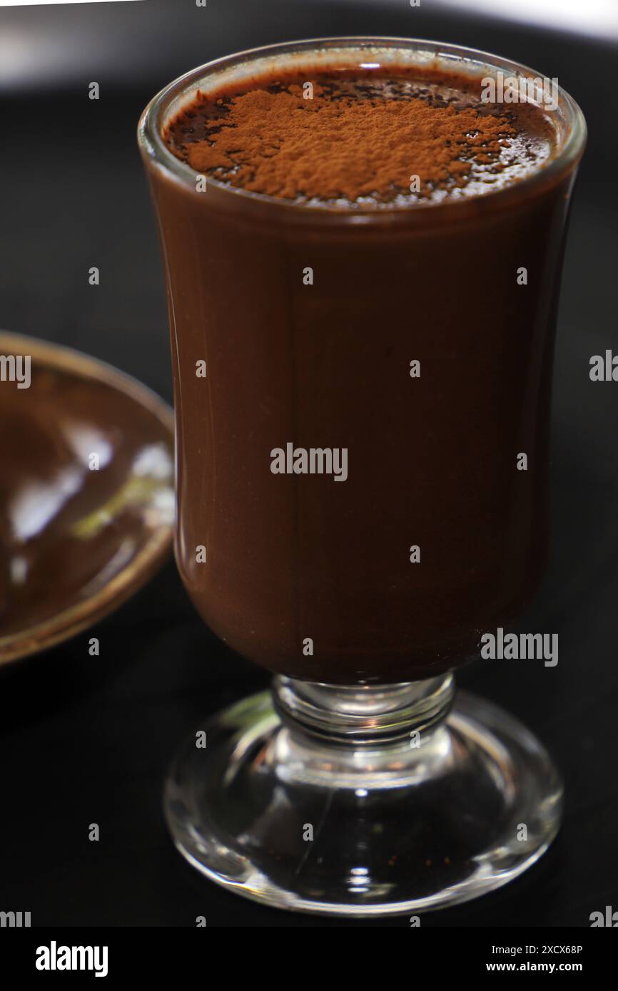 Un primo piano di un bicchiere pieno di ricca e cremosa bevanda al cioccolato condita con cacao in polvere Foto Stock