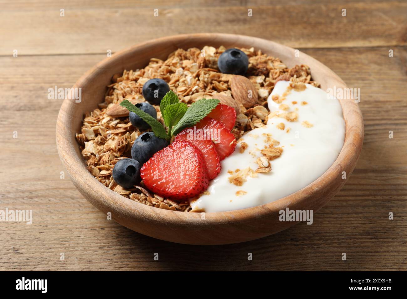 Gustose muesli con frutti di bosco, mandorle e yogurt in ciotola su un tavolo di legno, primo piano Foto Stock