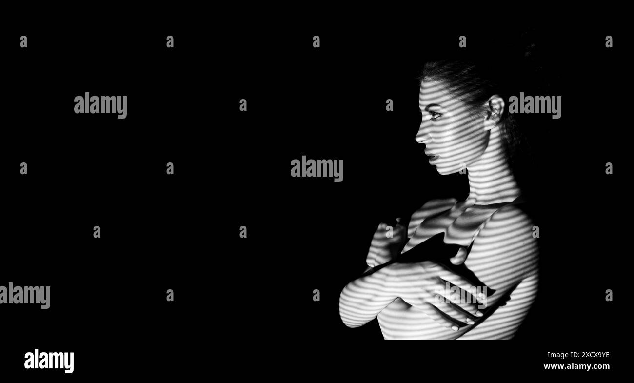Donna che posa con proiezione di luce a righe in una stanza buia Foto Stock