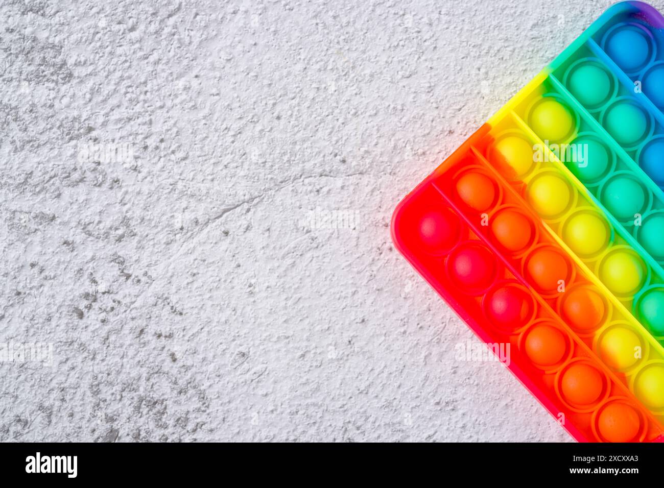 Vista dall'alto del giocattolo sensoriale anti-stress arcobaleno, premi e fallo passare su uno sfondo in pietra Foto Stock