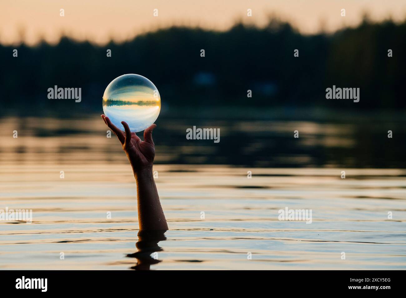 Mano di una persona che regge la sfera di cristallo che fuoriesce dal lago Foto Stock