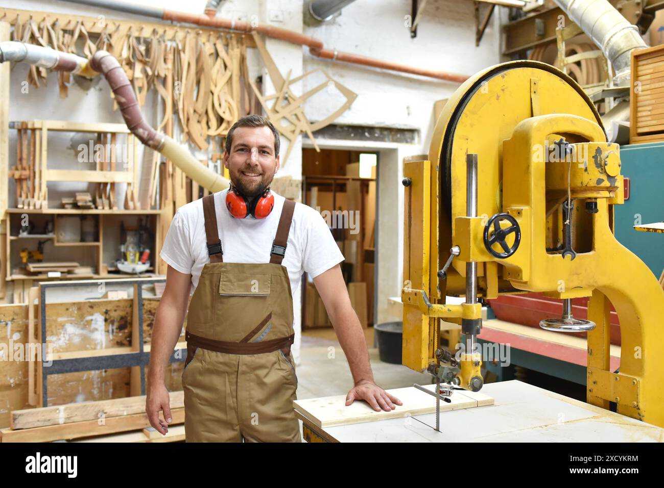 Ritratto di un falegname in abiti da lavoro e di protezione dell'udito in officina di una bottega del falegname Foto Stock