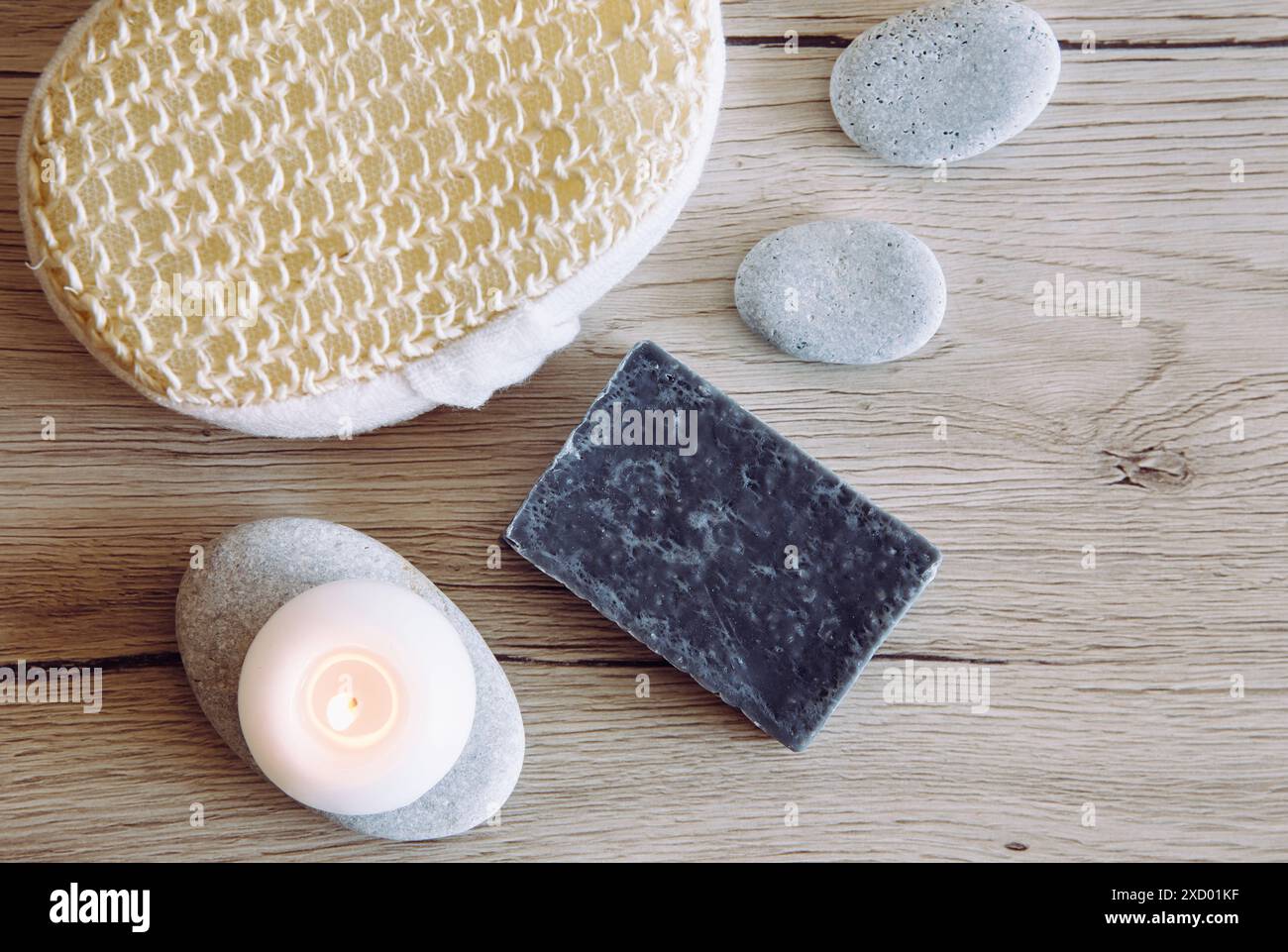 Vista piatta del sapone di argilla di colore grigio fatto a mano su sfondo in legno con candelabro e spugna da bagno, pietre marine piatte. Bagno di casa. Foto Stock