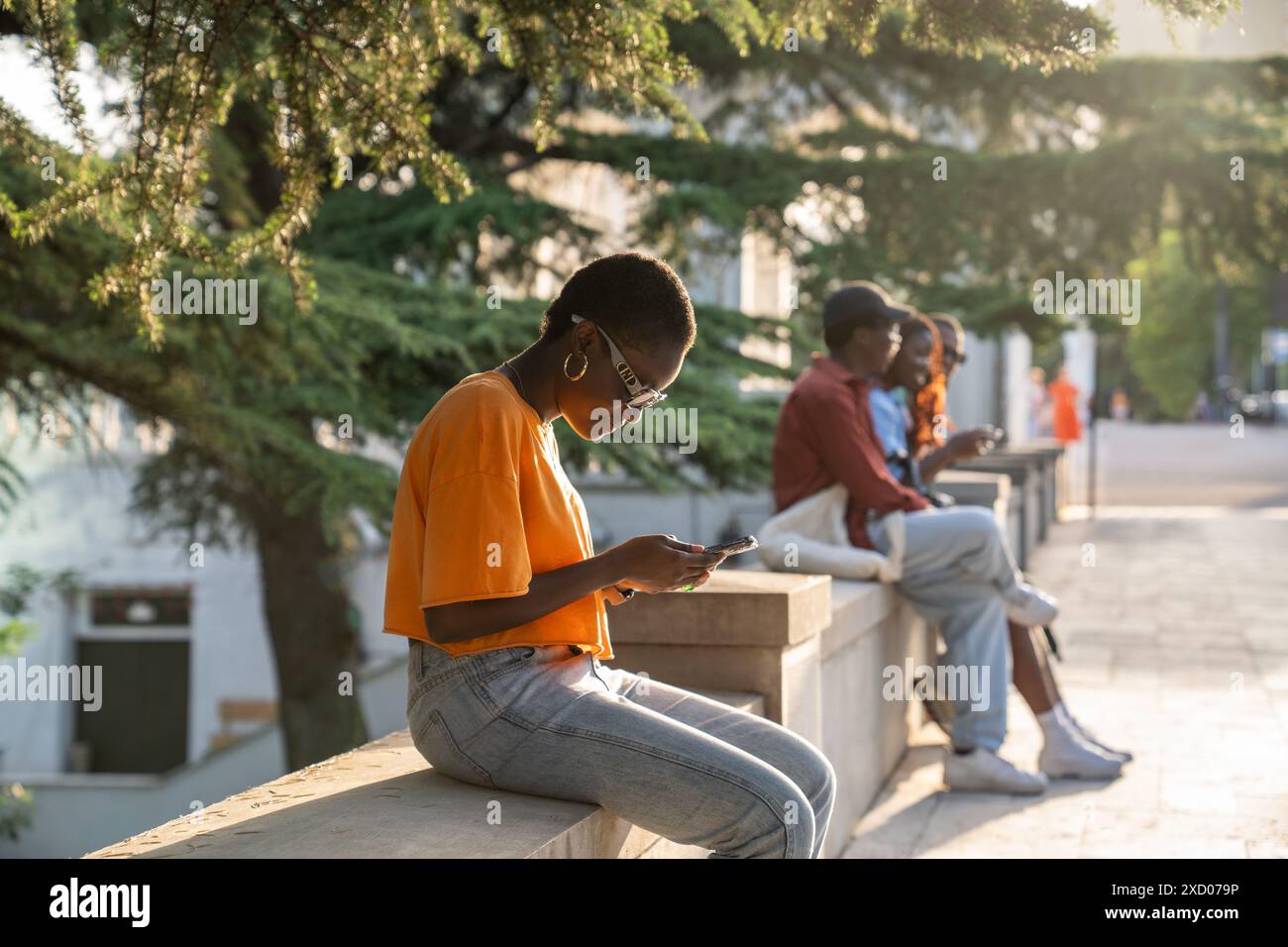 Focalizzata sullo schermo, studentessa afroamericana siede da sola all'aperto sui social media web a scorrimento. Foto Stock